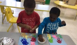 Two children doing a craft with handprints and small objects