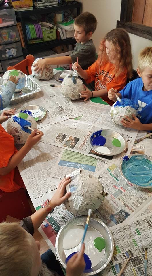 Children painting paper mache globes at a table covered with newspaper