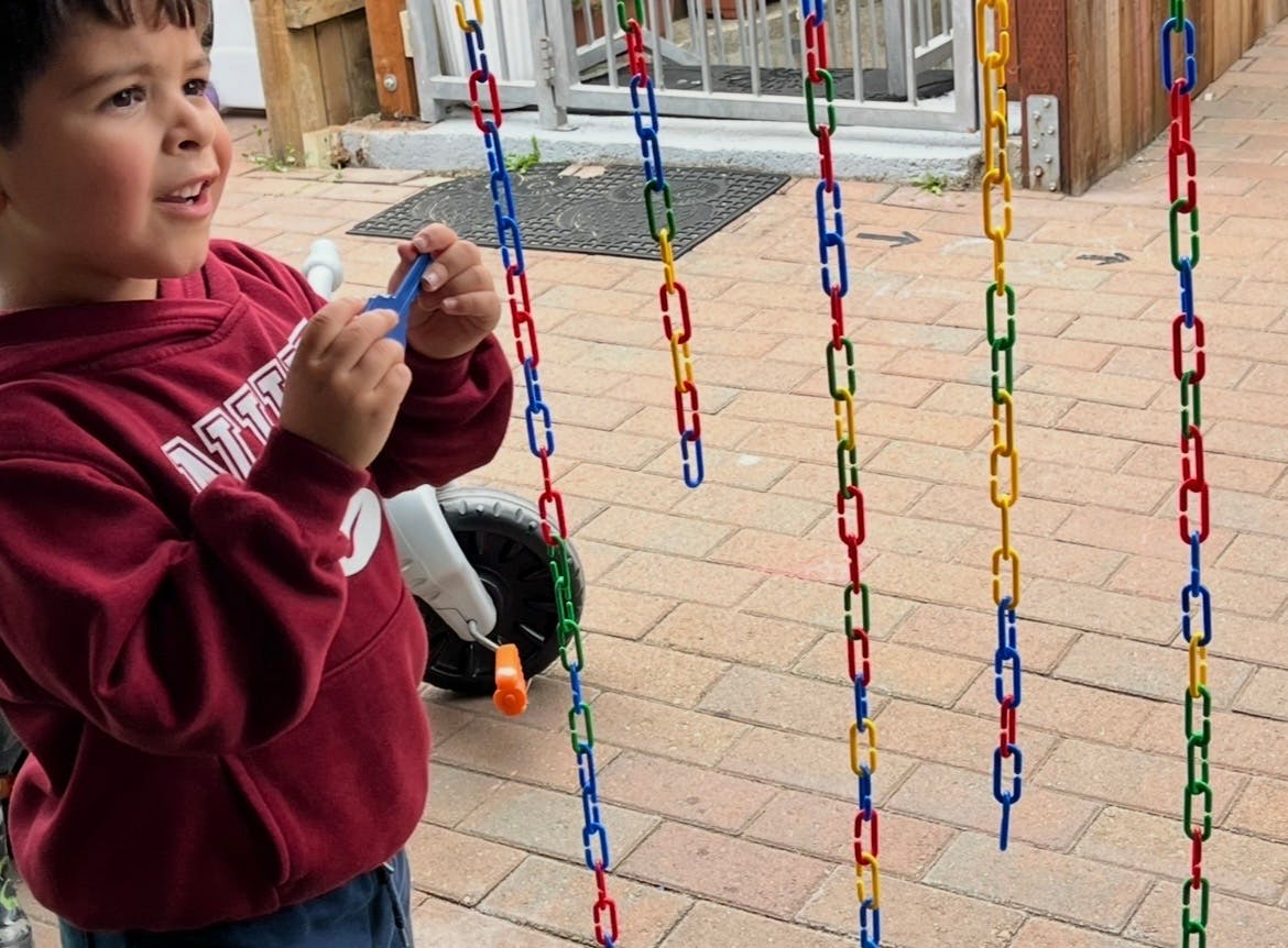 Child in a maroon sweatshirt holding a blue toy link next to colorful chain toys