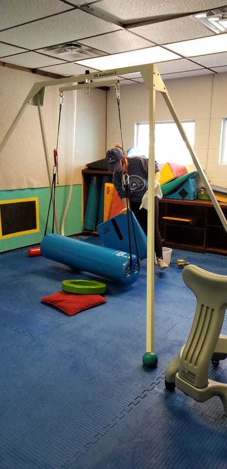 Person cleaning a therapy room with a swing and padded floor