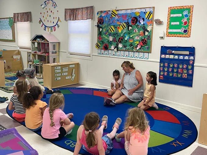An adult and several children sitting on a rug in a classroom