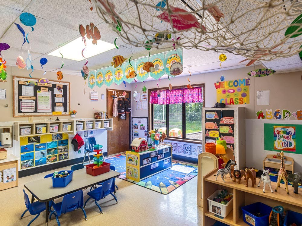 An empty colorful classroom decorated for children with tables, chairs, and learning materials