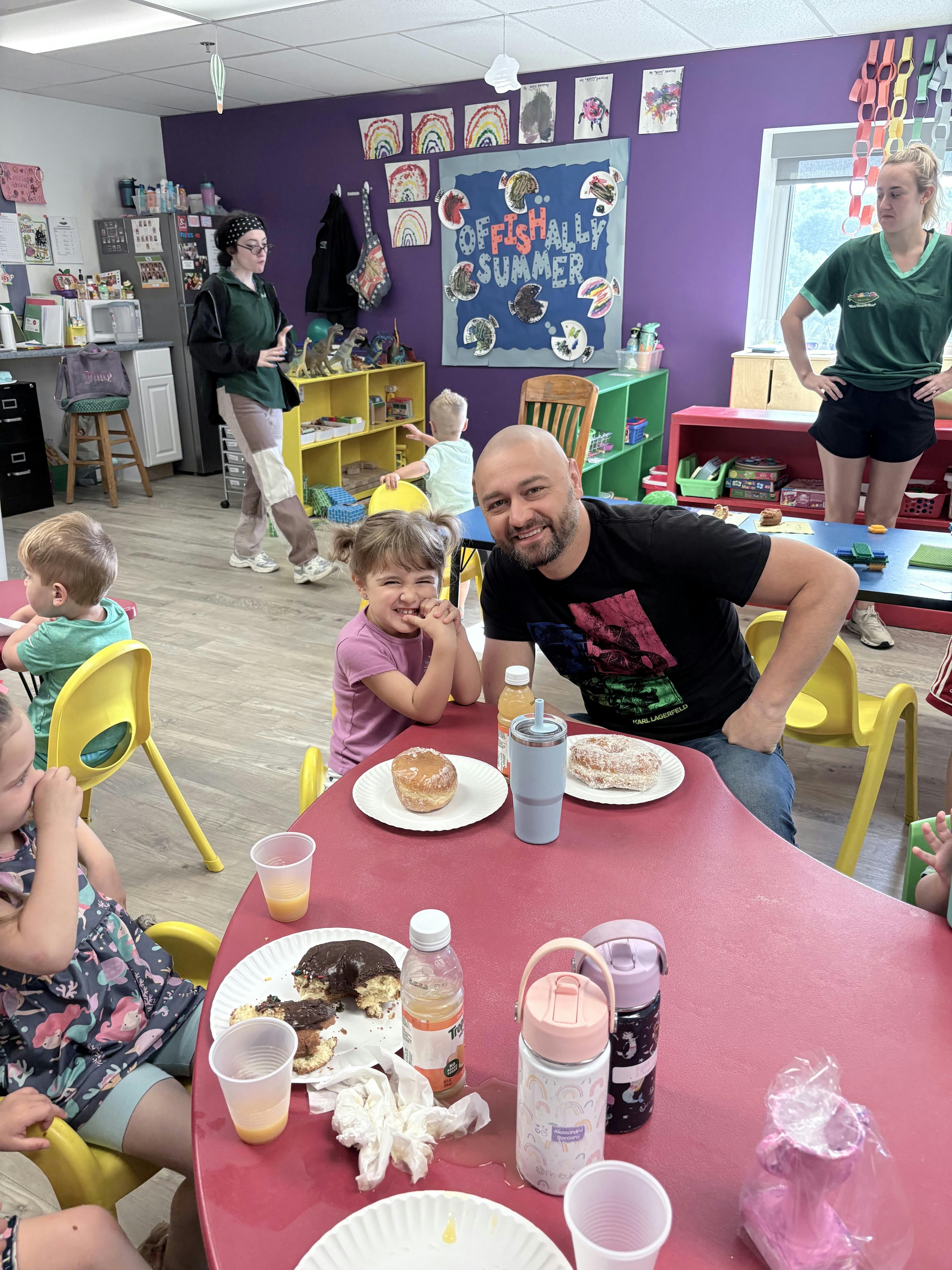 A person and a child sitting at a table with donuts in a classroom