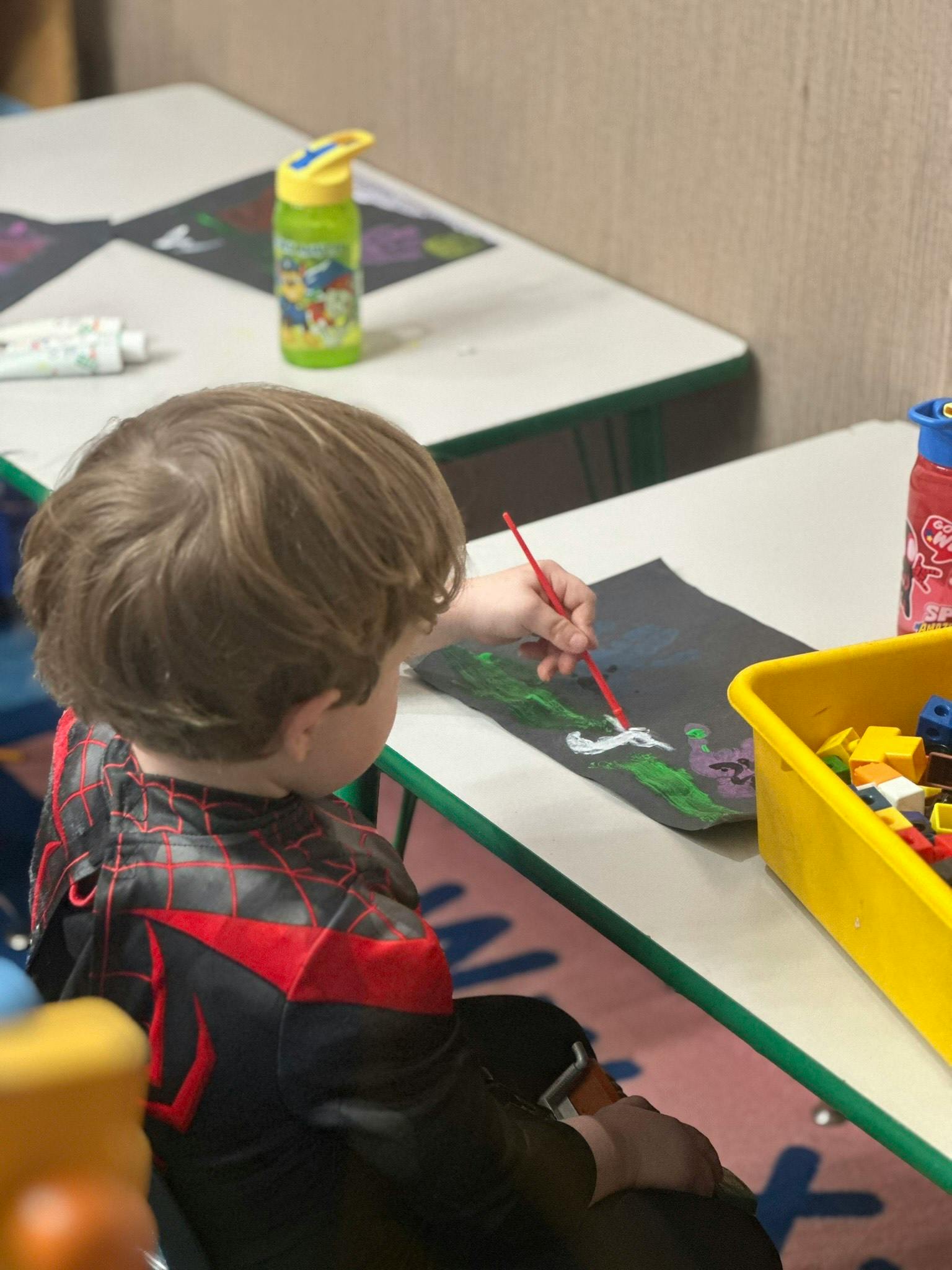 Child painting on a black paper with a red brush