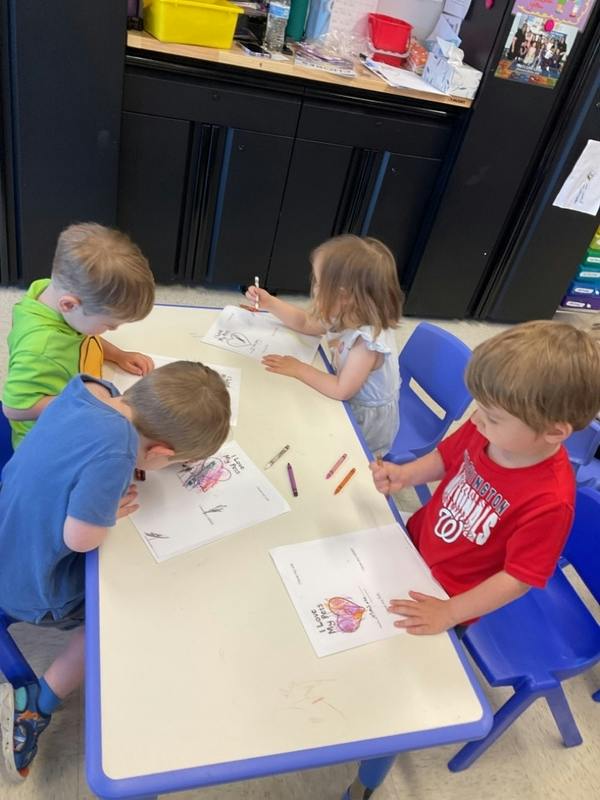 Four children drawing at a table in a classroom