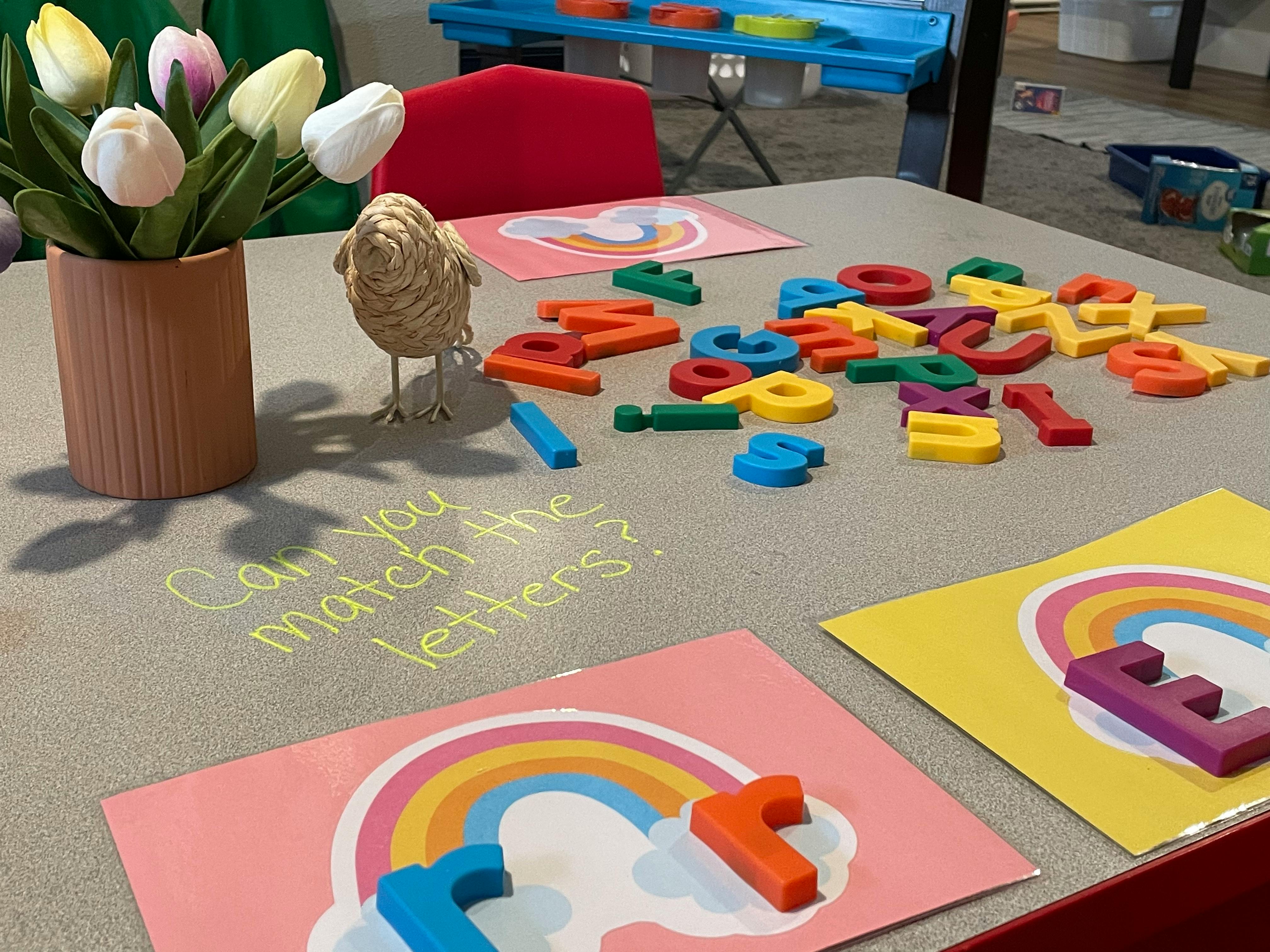 Table with colorful magnetic letters, rainbow cards, and text "Can you match the letters?"