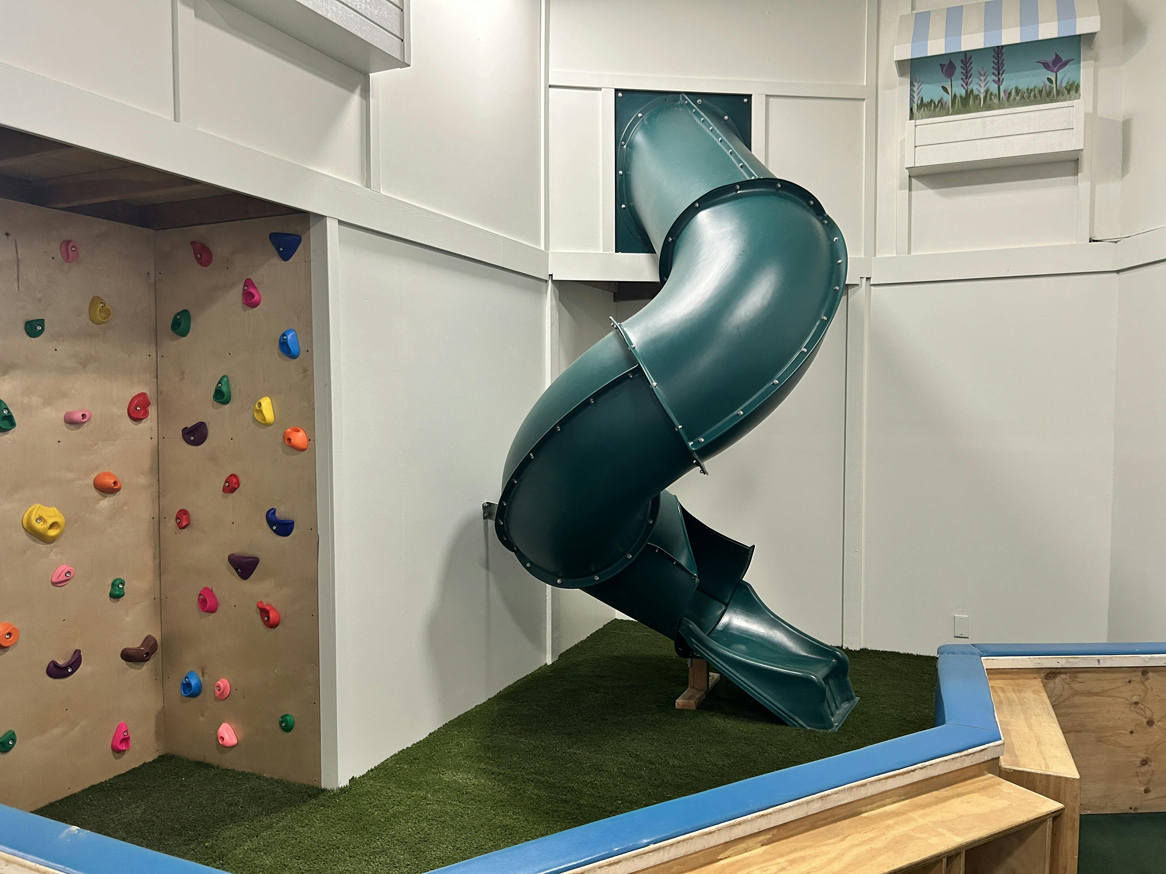 Indoor play area with a green slide and a rock climbing wall