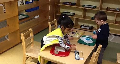 Two children playing with items at a small table in a classroom
