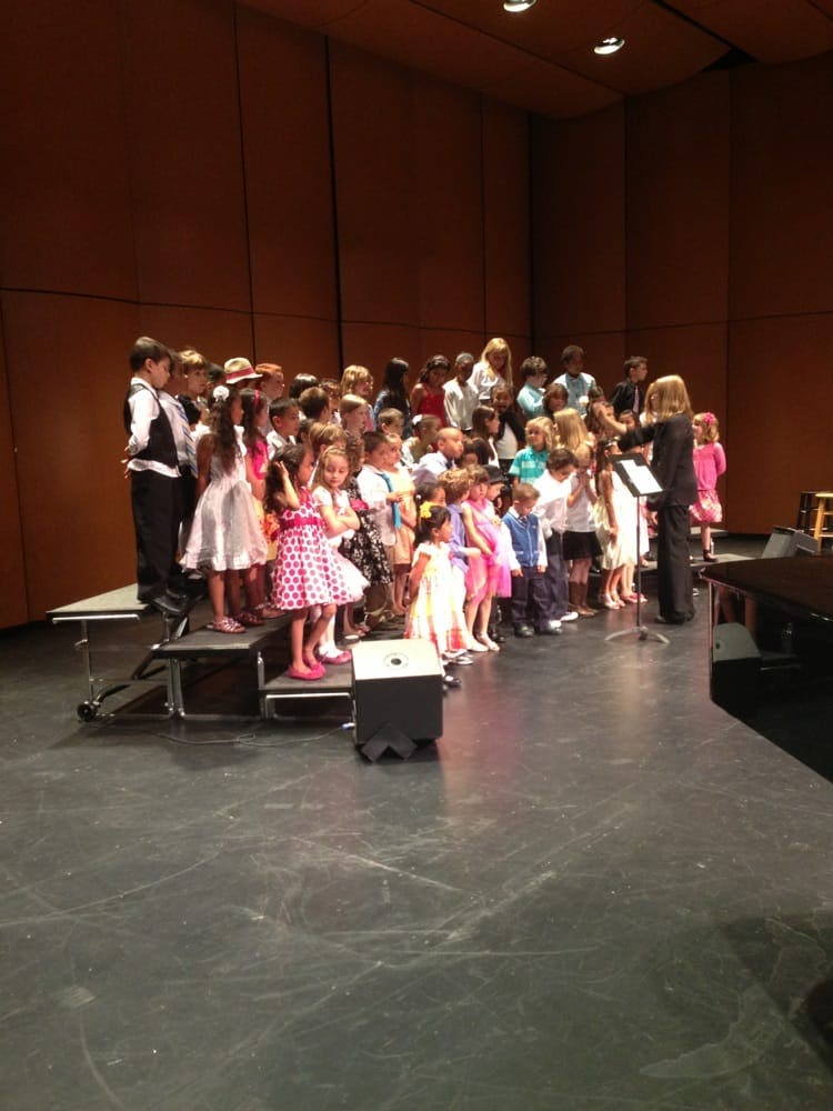 Children on risers with an adult conductor on a stage