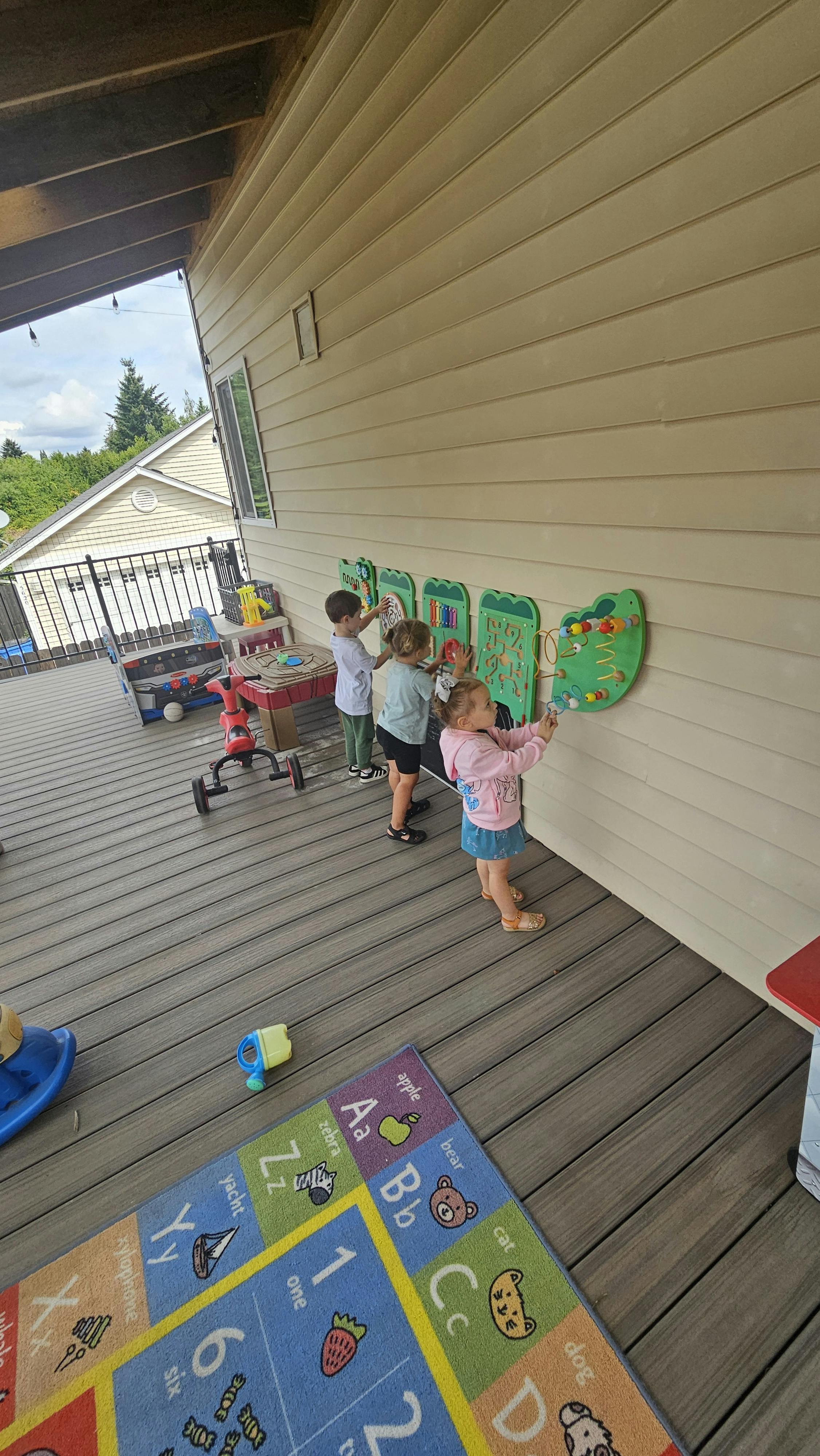 Three children playing with wall-mounted activity boards on a deck