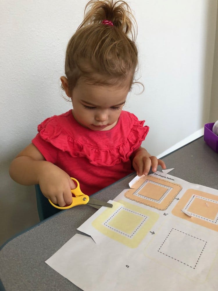 Child cutting paper with scissors at a table
