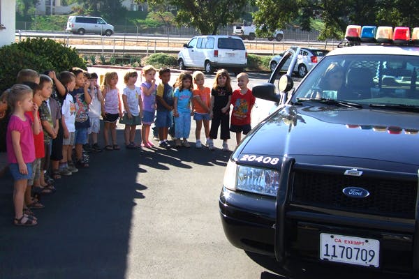 Children standing in a line next to a police car
