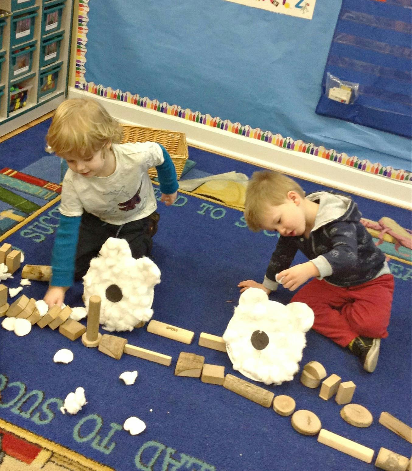 Two children playing with blocks and cotton shapes on a blue rug