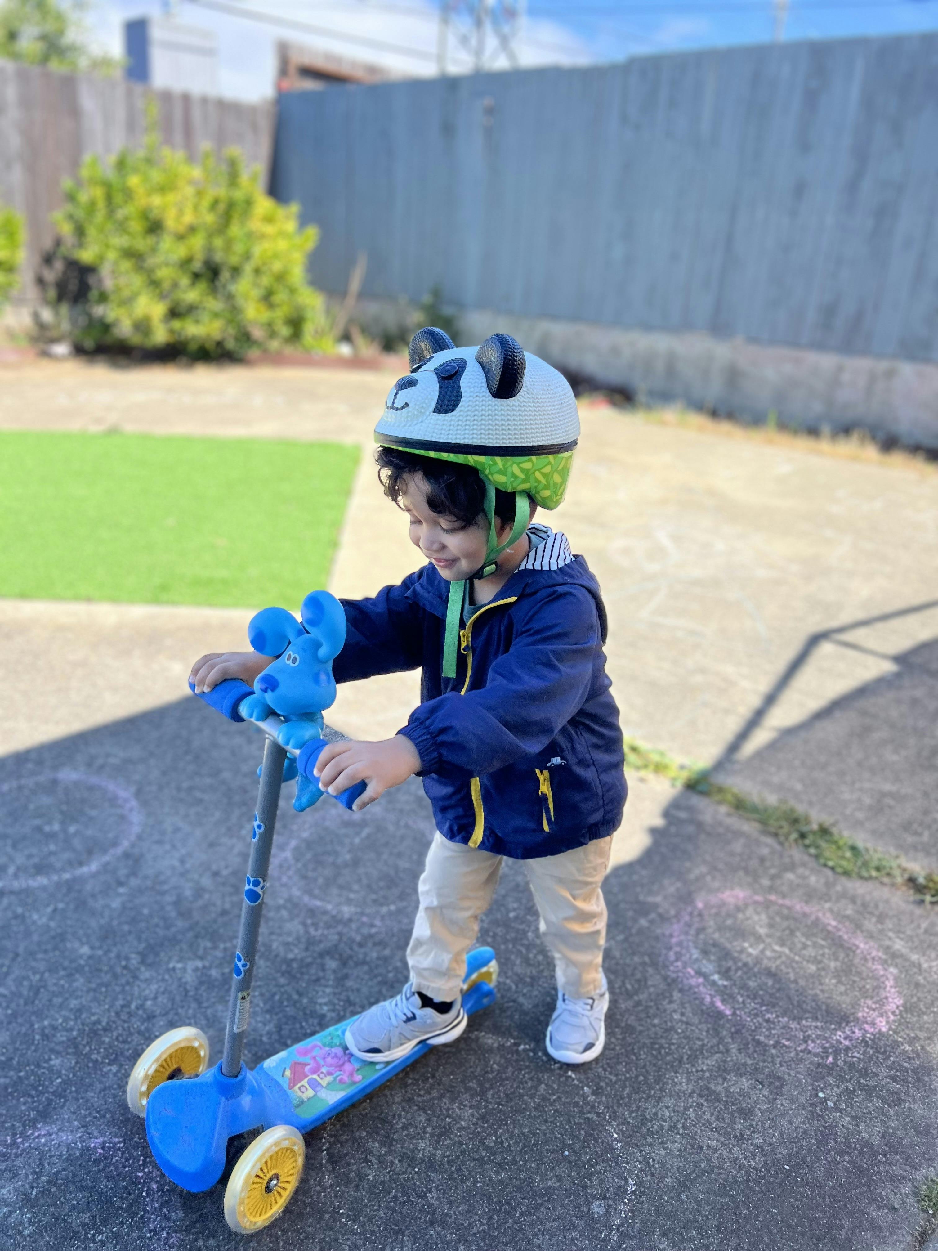 Child wearing a panda helmet standing on a scooter