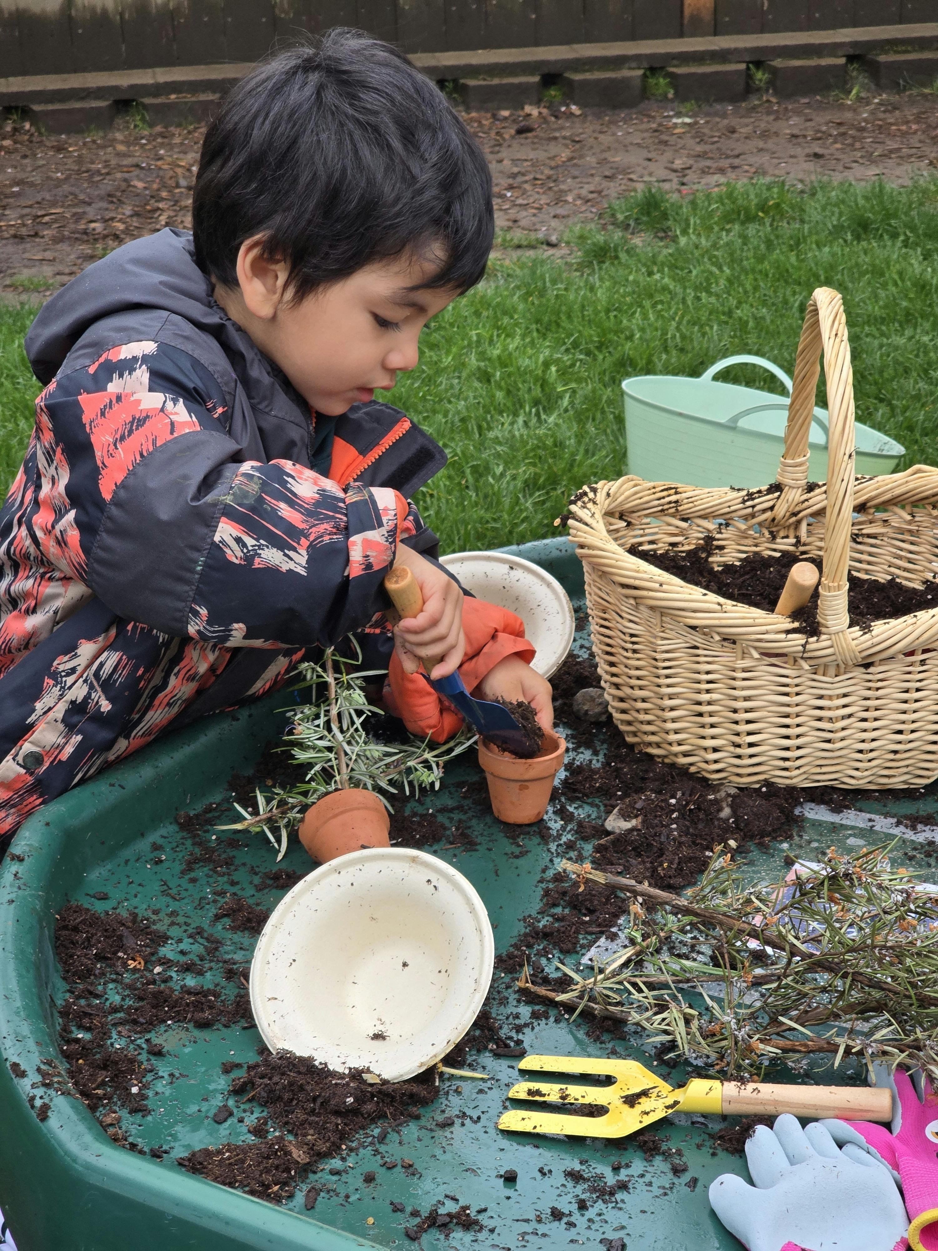 Child putting soil into a small terracotta pot with a trowel