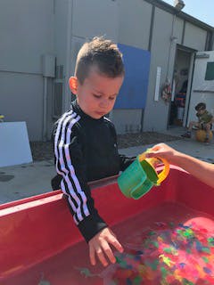 Child playing with water and toys in a red bin