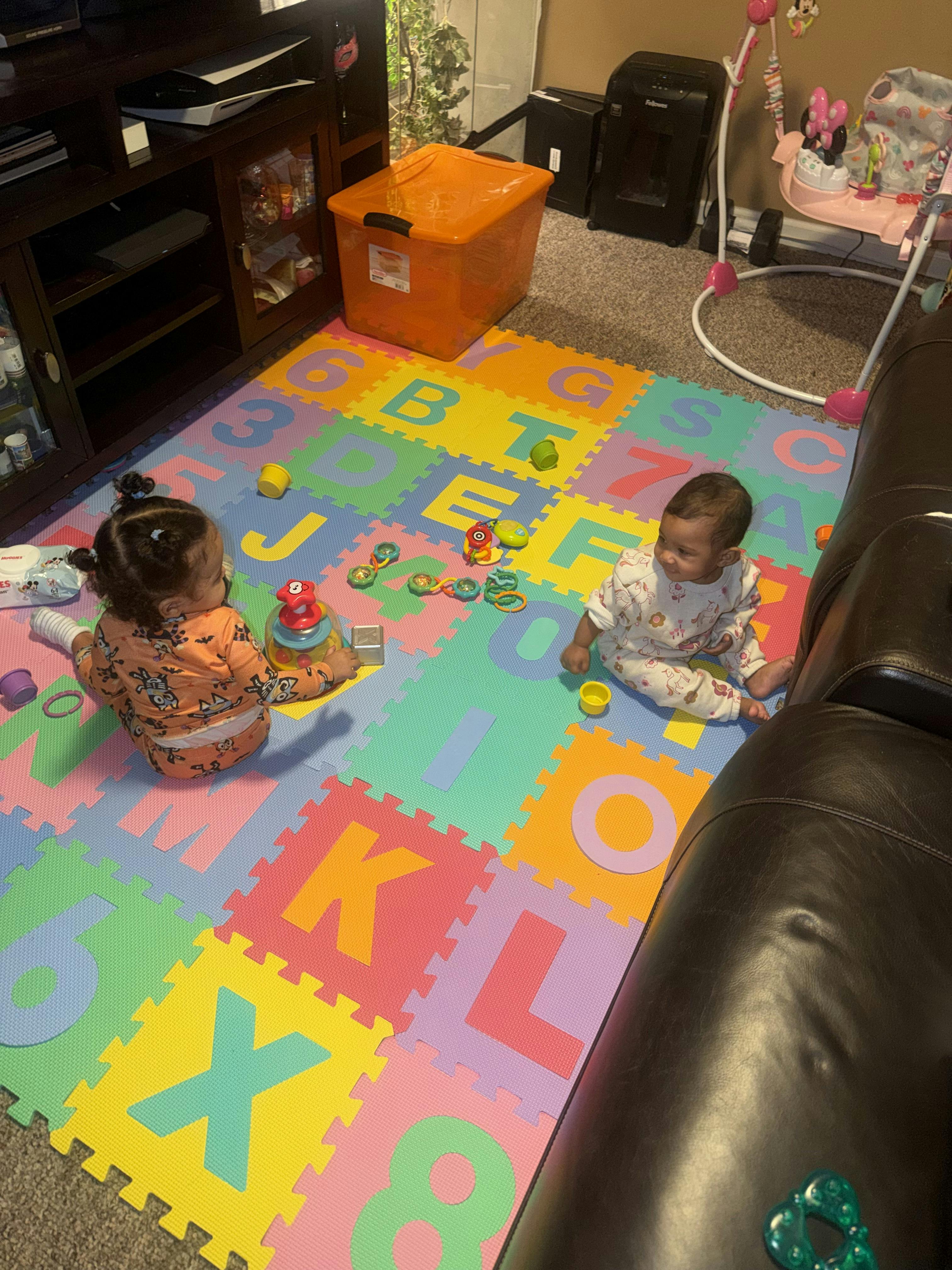Two infants playing with toys on a colorful alphabet and number playmat