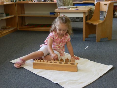 Child playing with wooden cylinder blocks on a mat in a classroom
