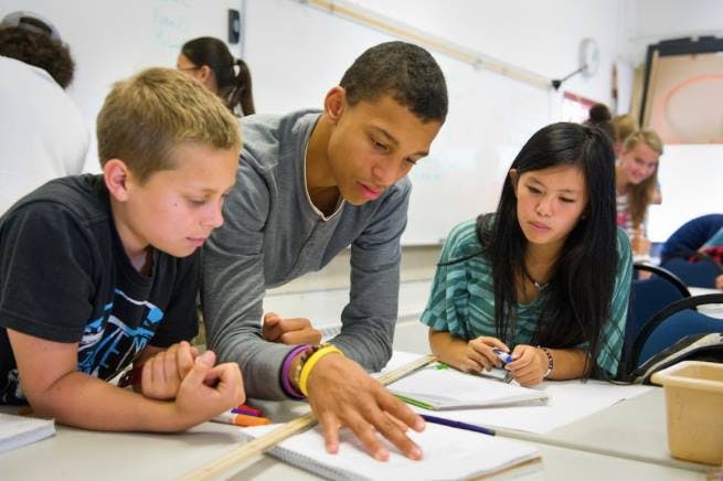 Three teens and a child looking at a notebook in a classroom