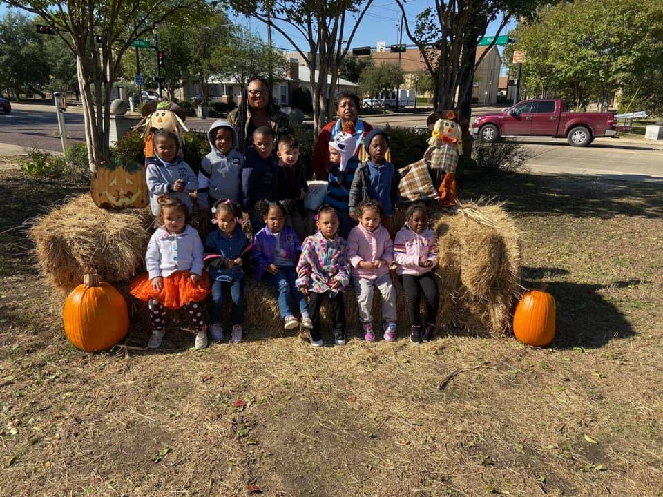 Adults and children sitting on hay bales with pumpkins