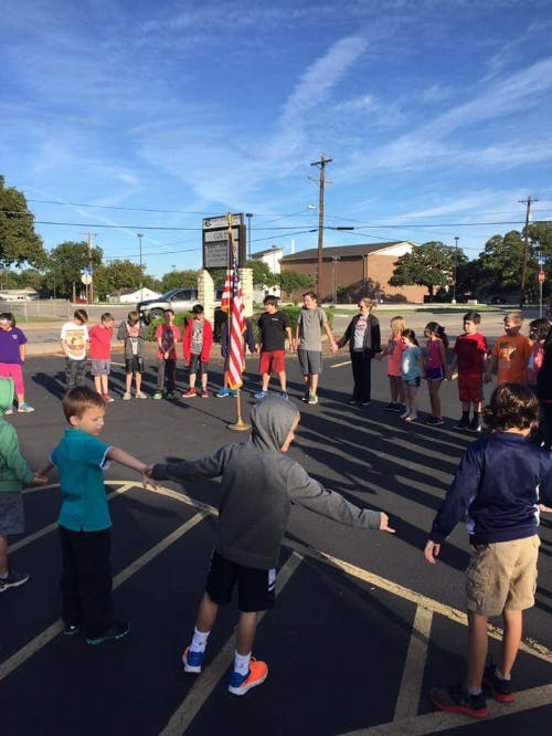 Children holding hands in a circle around an American flag