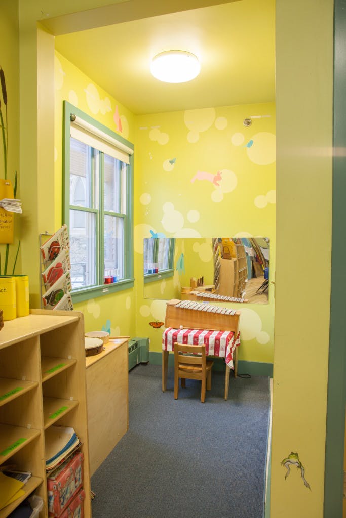 A classroom with yellow walls, a window, and a small table with a chair