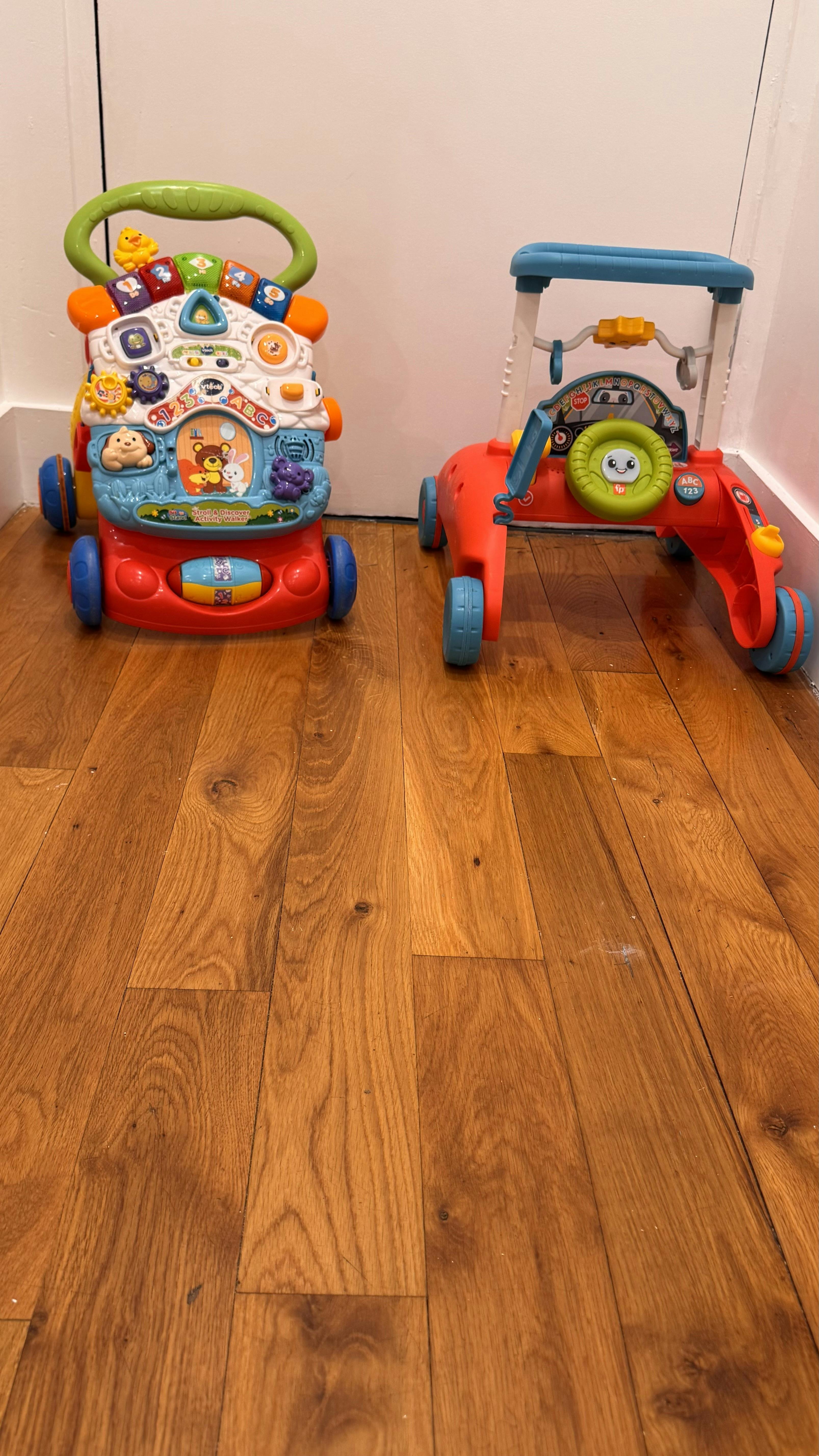 Two colorful baby walkers with activity panels on a wooden floor