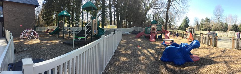 Outdoor playground with slides, climbing structures, and a white fence