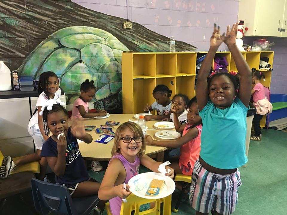 Children in a classroom, one child with arms raised, another holding a plate