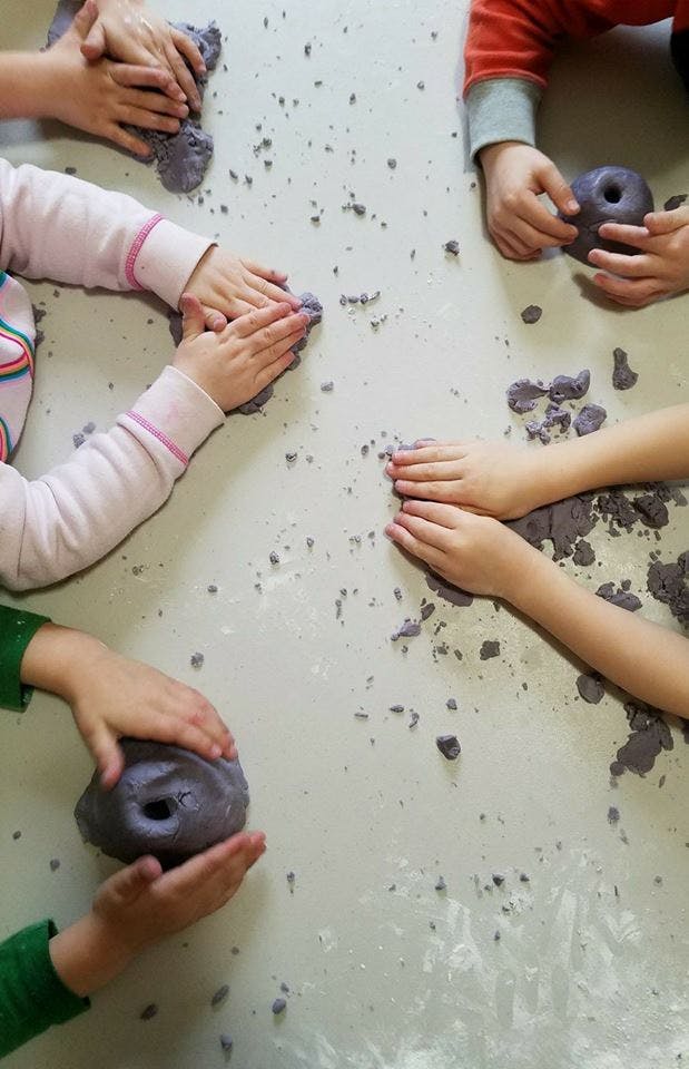 Multiple children's hands playing with purple kinetic sand on a table