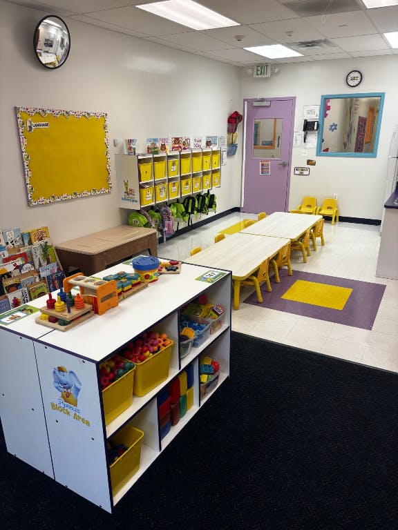 Preschool classroom with small tables and chairs, toy storage, and cubbies