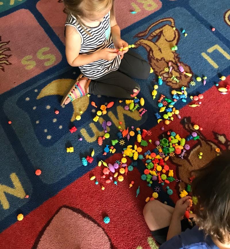 Two children playing with colorful small toys on a patterned rug