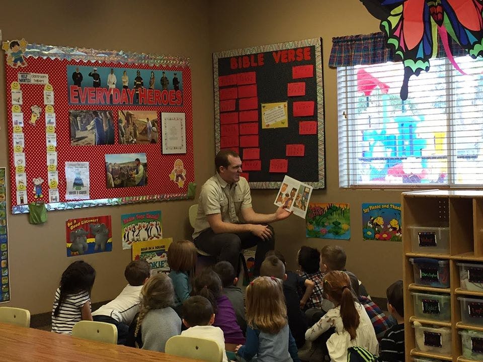 Adult reading a book to a group of children in a classroom