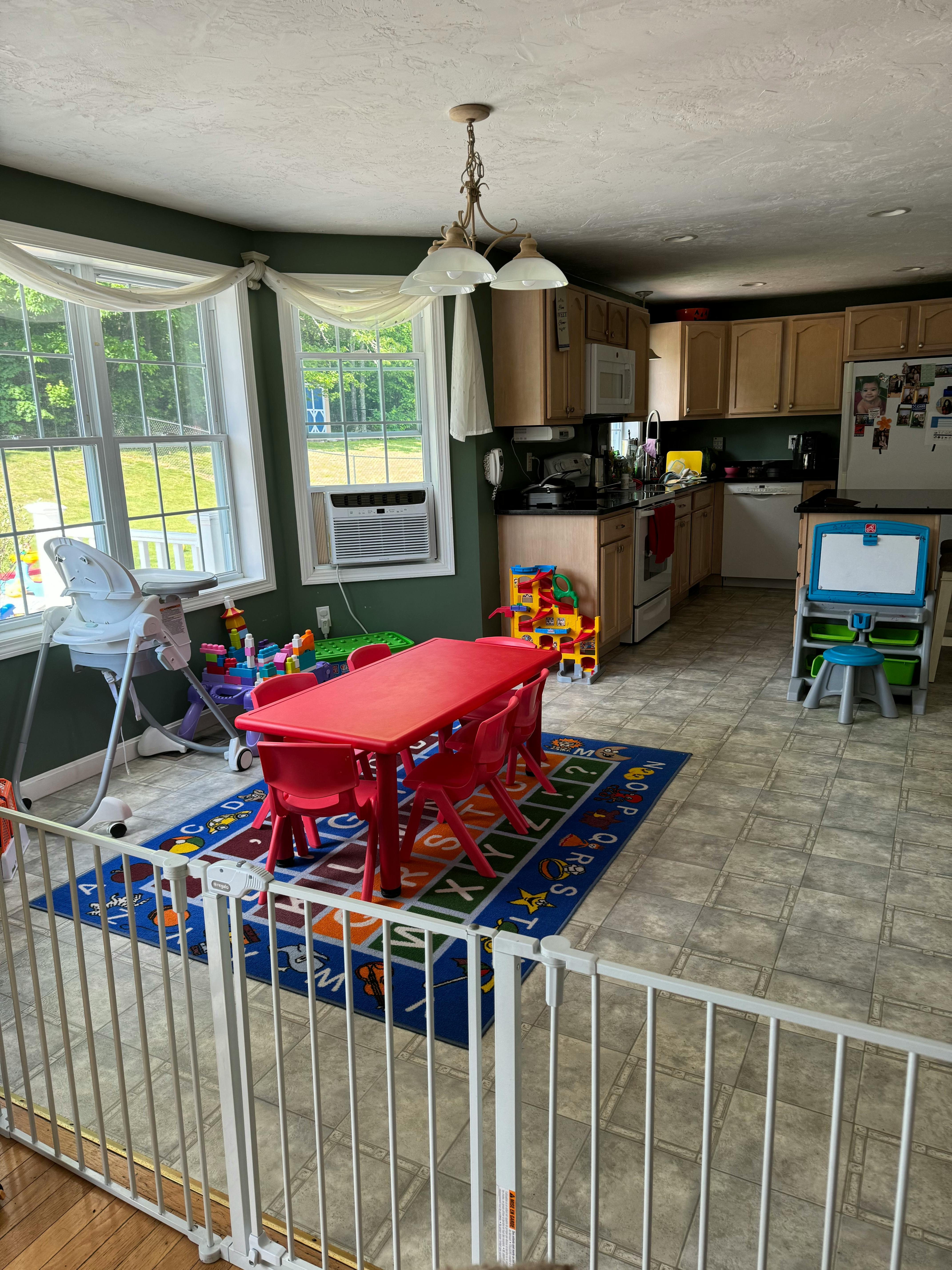 Play area with a red table and chairs on a blue rug, next to a kitchen