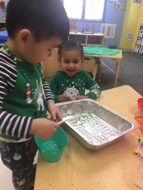 Two children playing with green sprinkles in a classroom