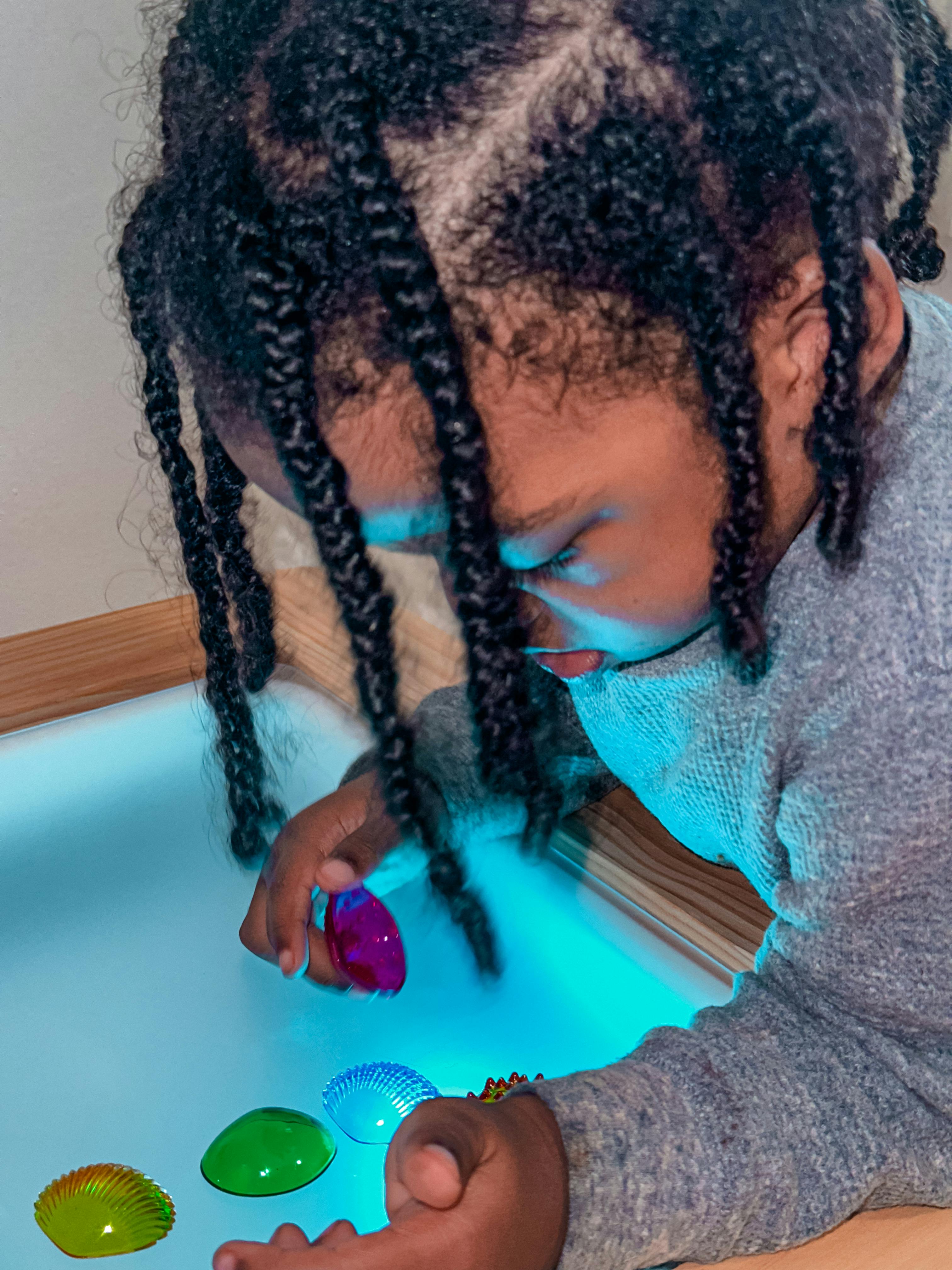 Child playing with colorful translucent shells in a light-up bin