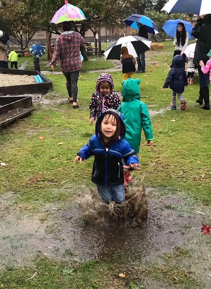 Child in a blue jacket jumping in a muddy puddle