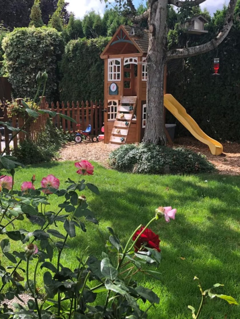 Playhouse with a slide next to a tree in a grassy yard