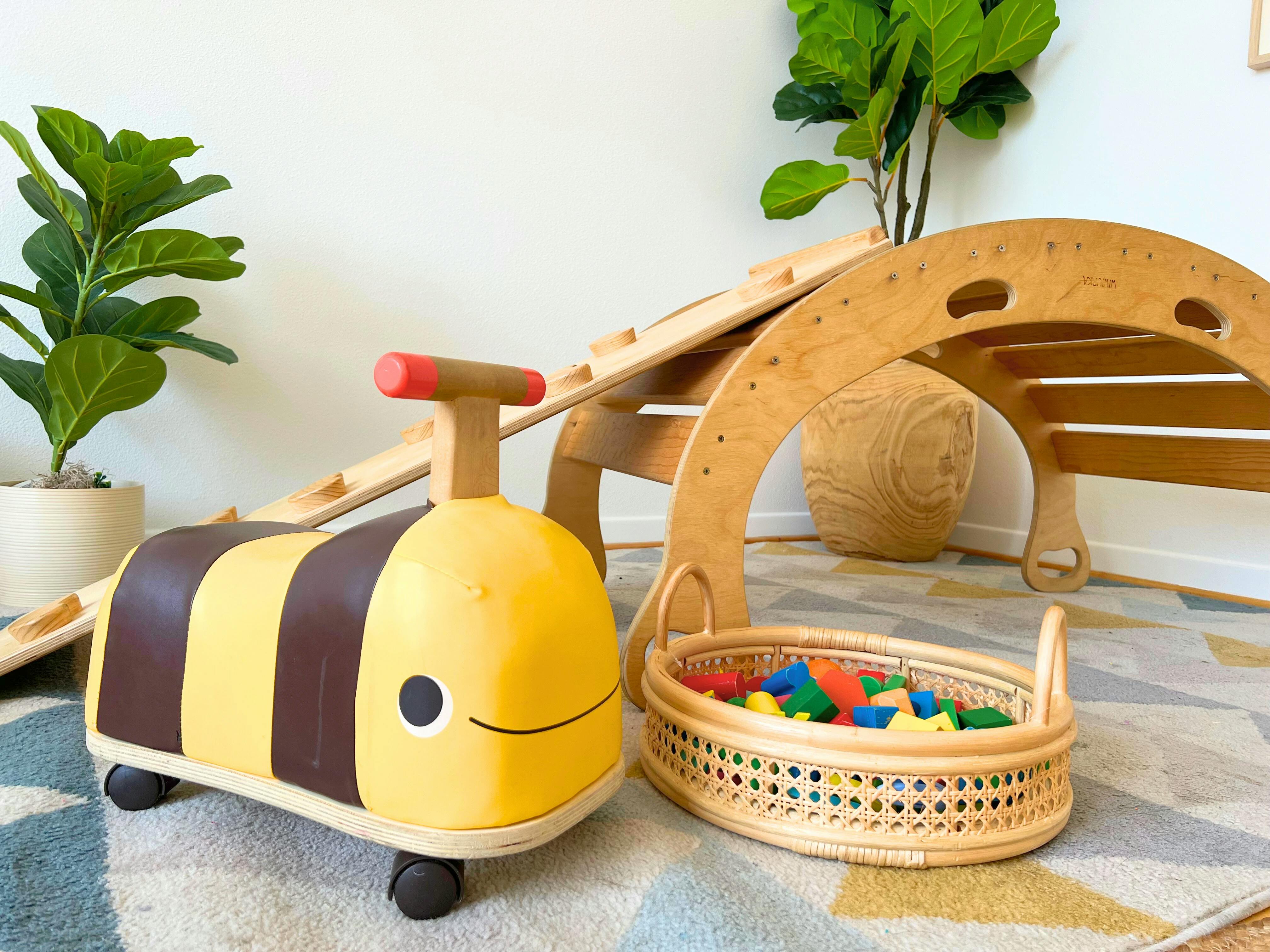 Yellow and brown ride-on toy next to a wooden climbing arch and basket of blocks