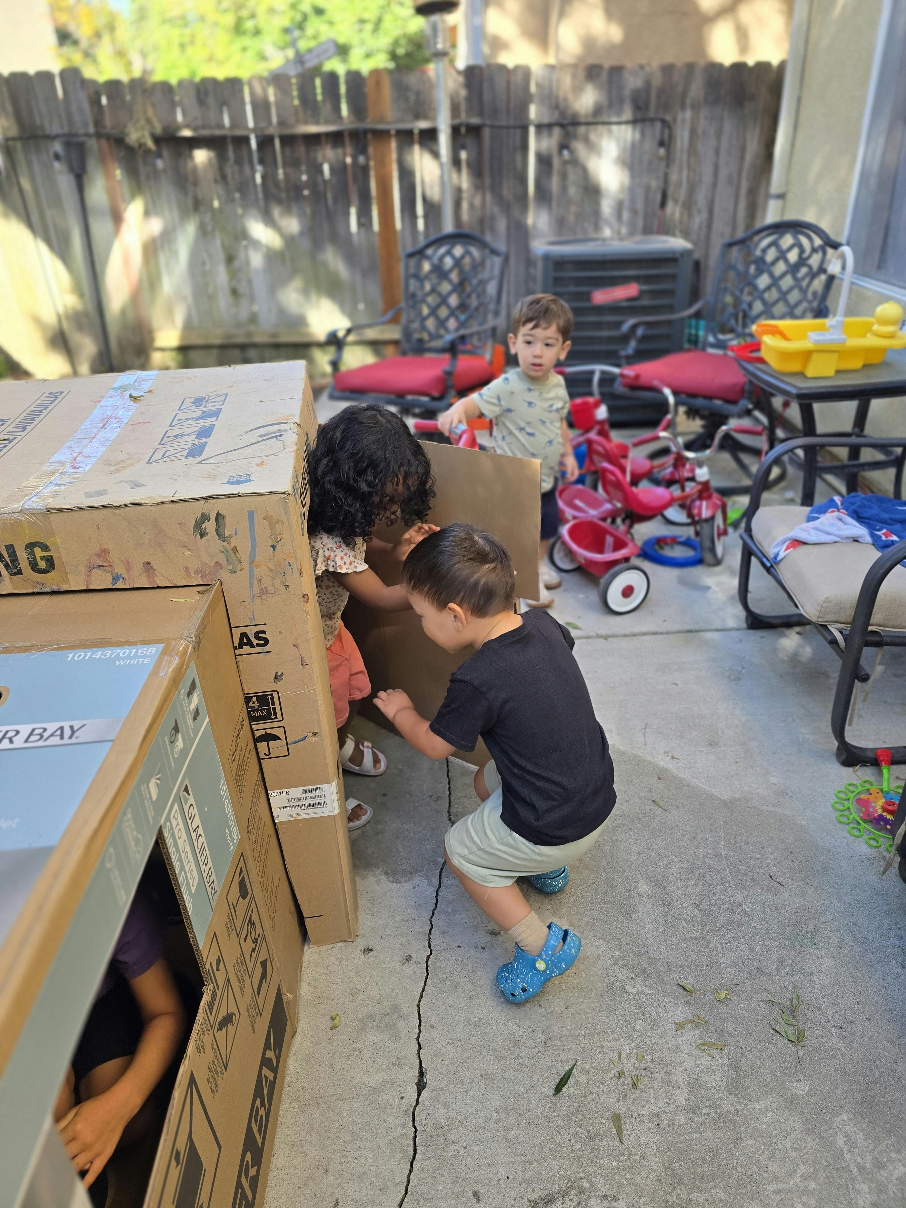Children playing with large cardboard boxes in a backyard