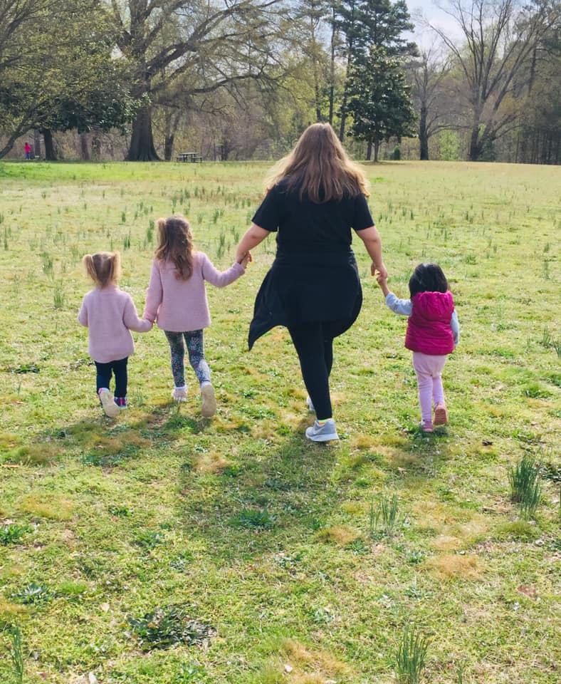 Person holding hands with two children and walking in a grassy field