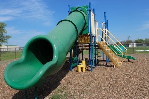 Green tube slide and yellow stairs on a playground