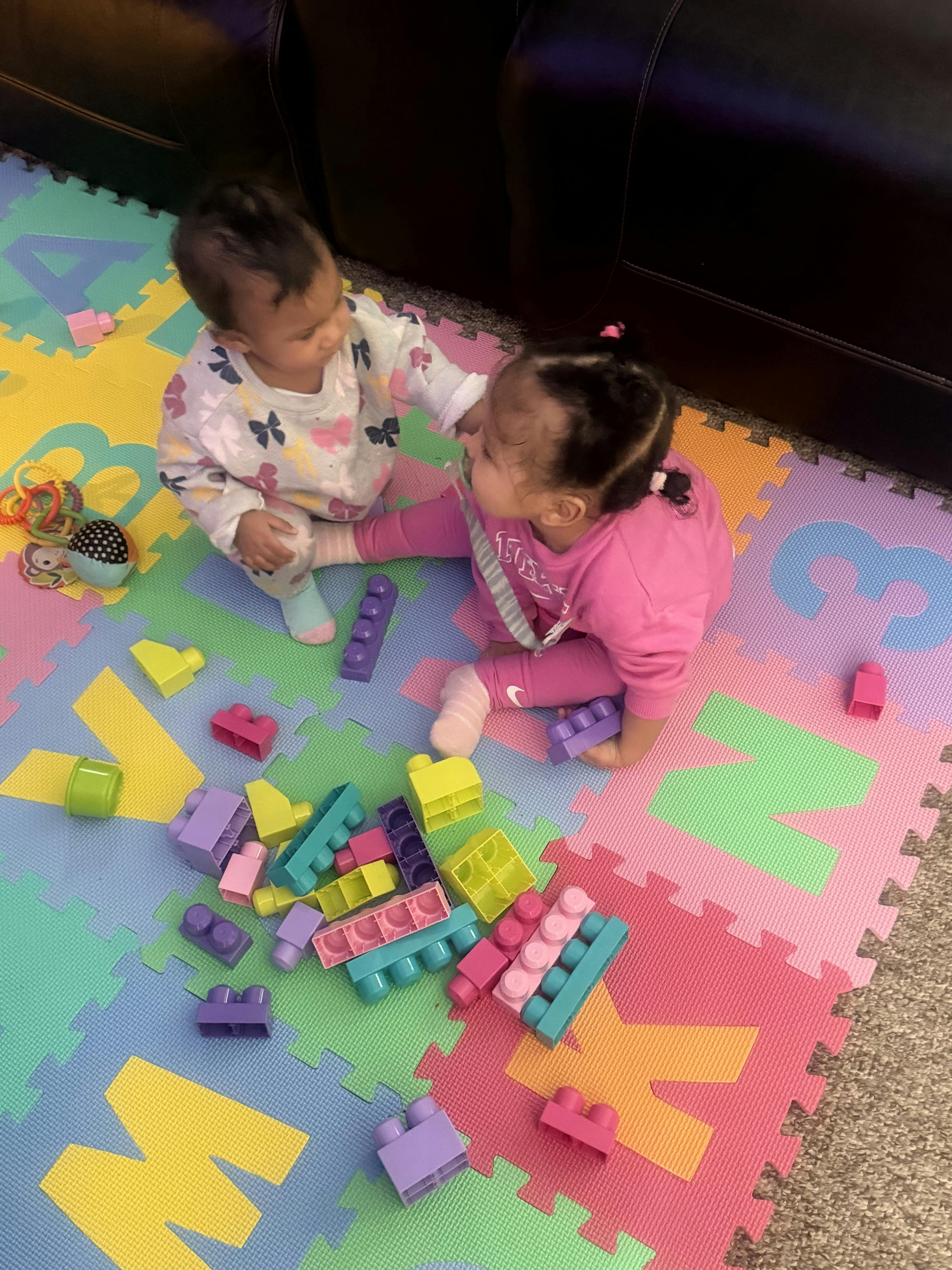 Two children playing on a colorful mat with building blocks