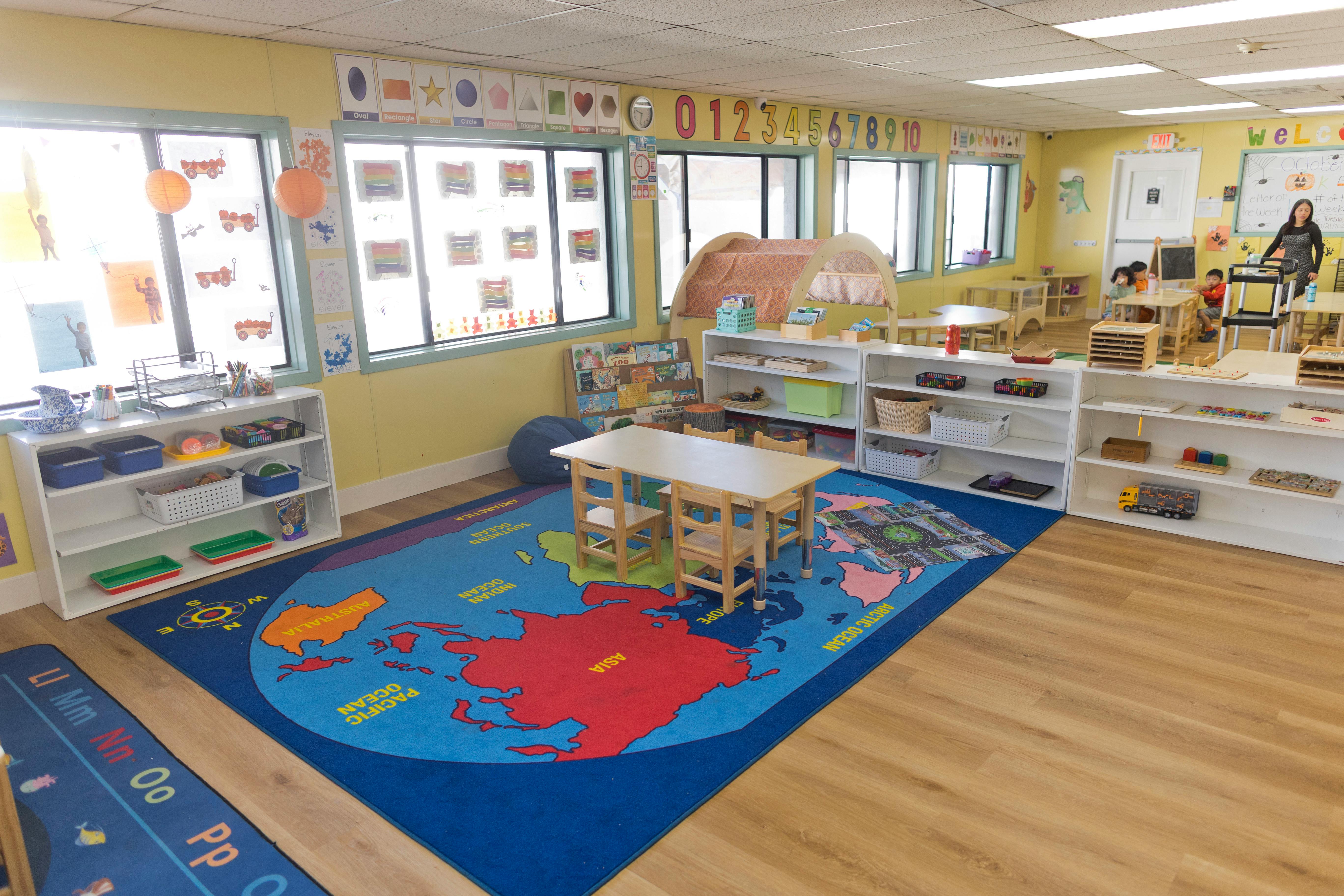 Classroom with map rug, small tables and chairs, shelves with toys, and windows
