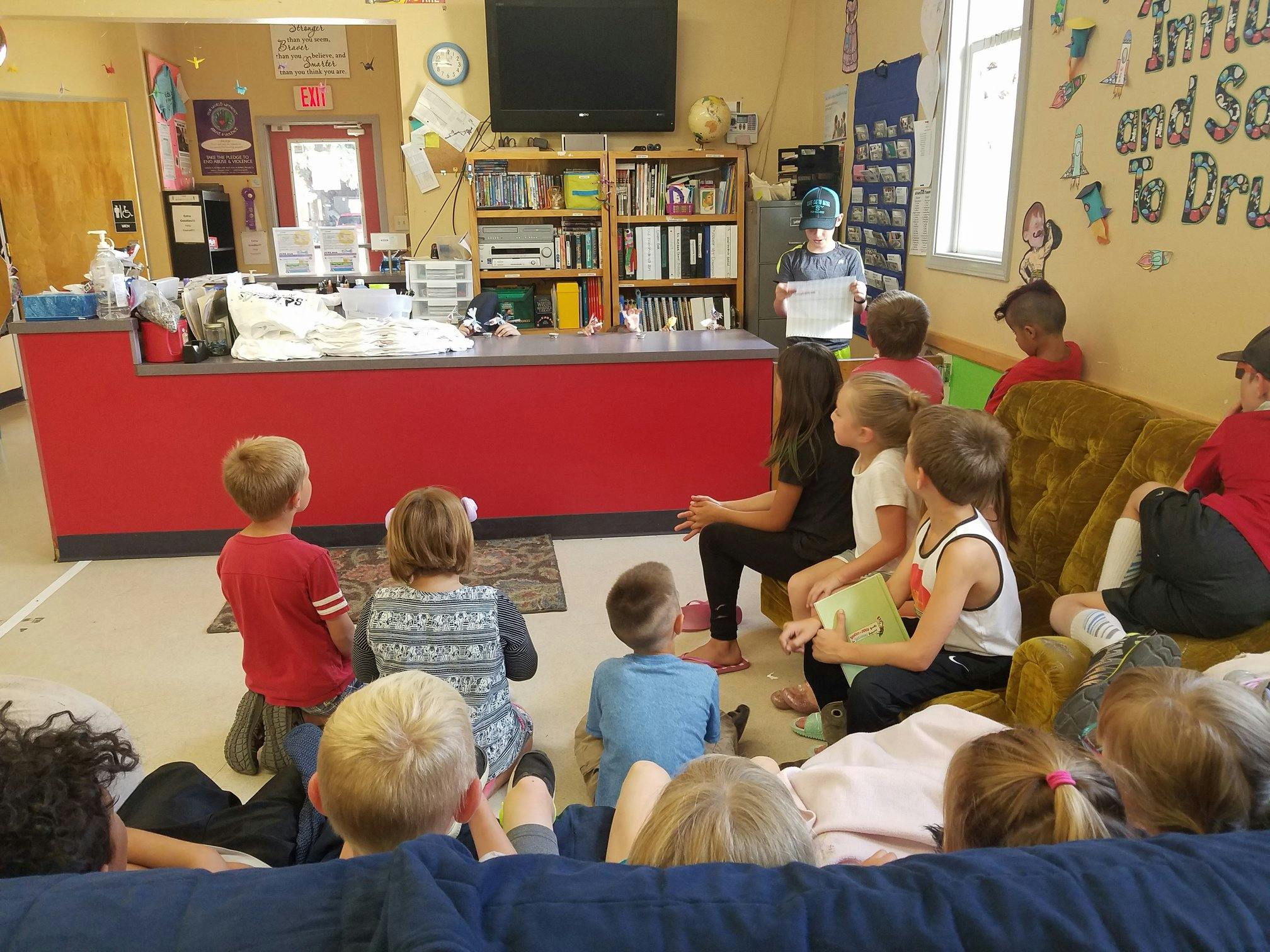 Adult and children gathered in a room, some sitting on floor, some on sofa