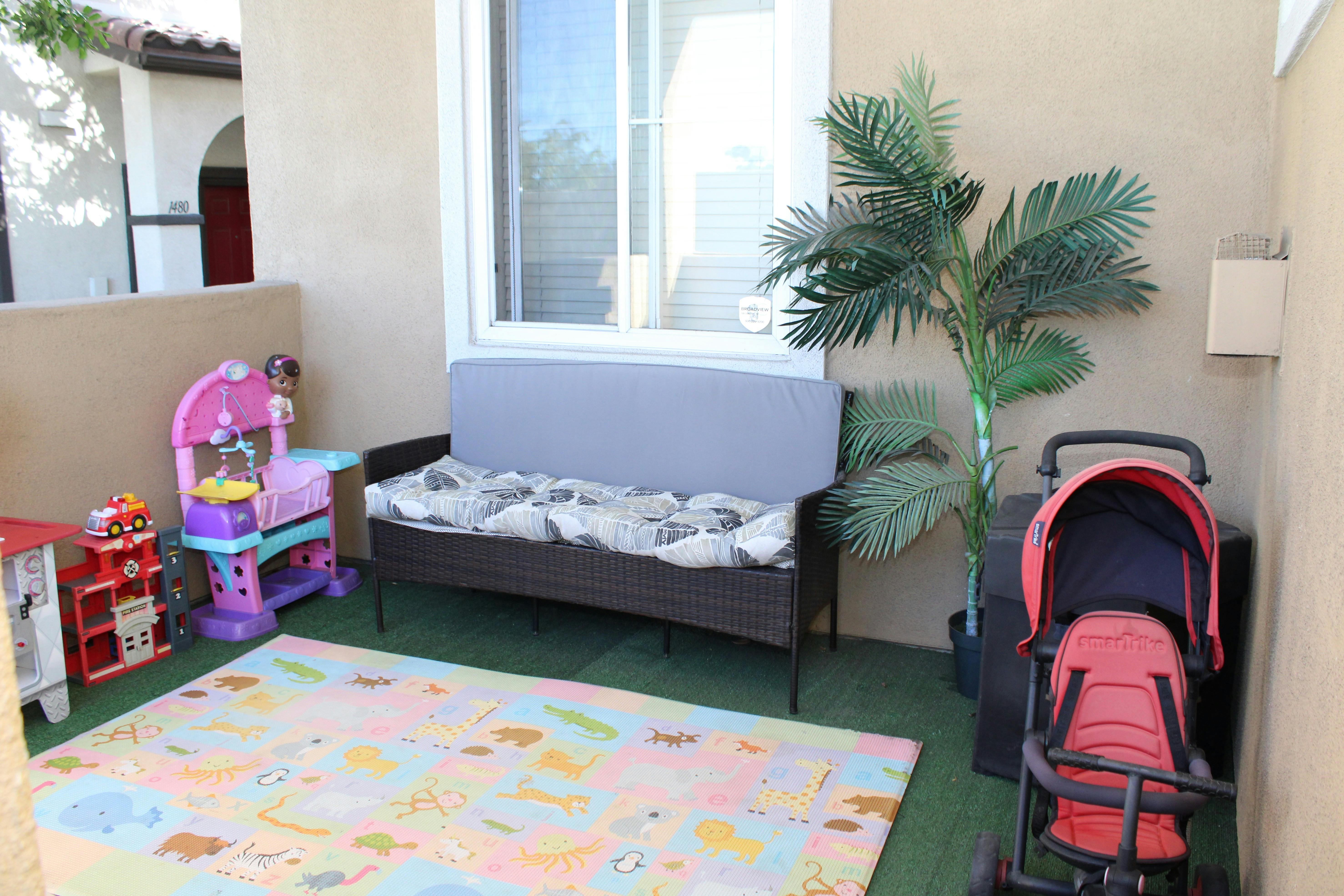 Outdoor patio area with a sofa, artificial plant, and toys on a play mat