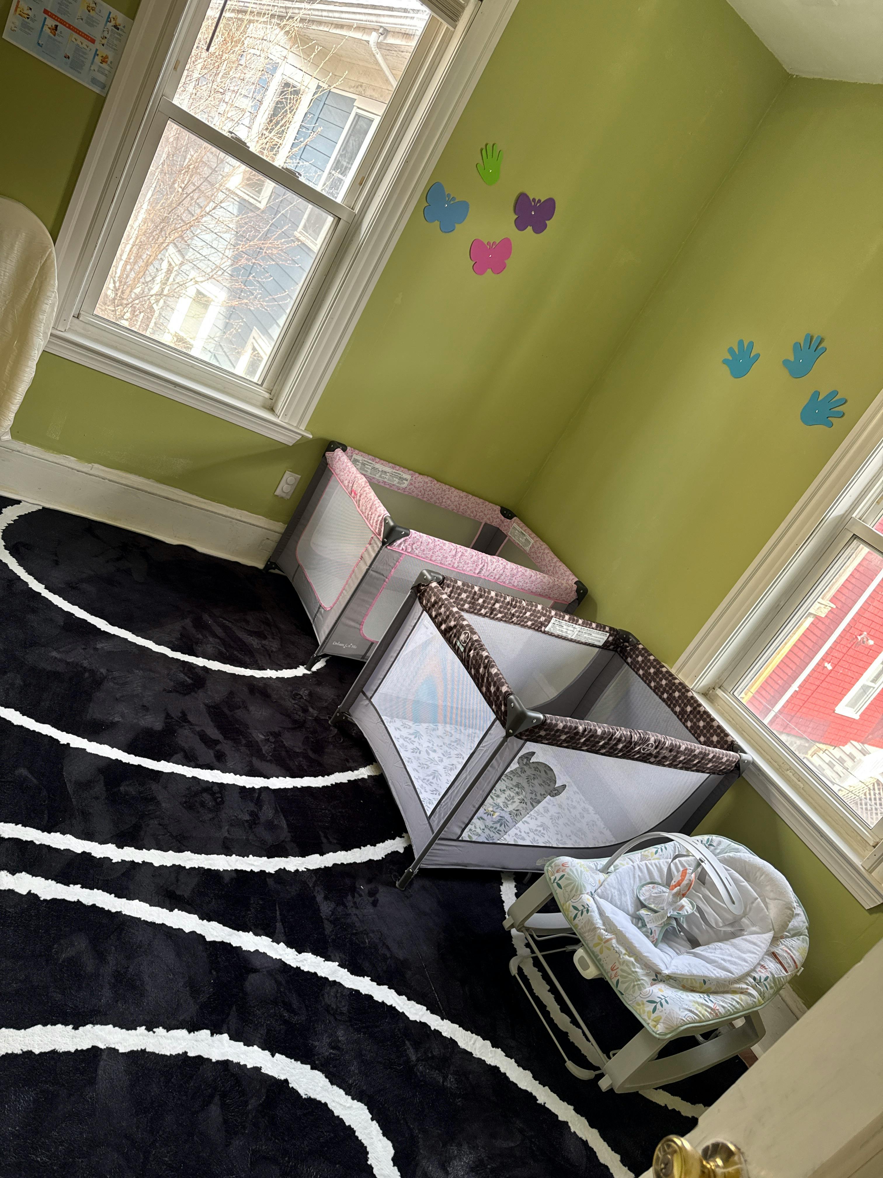 Playard and infant bouncer in a room with green walls and black rug