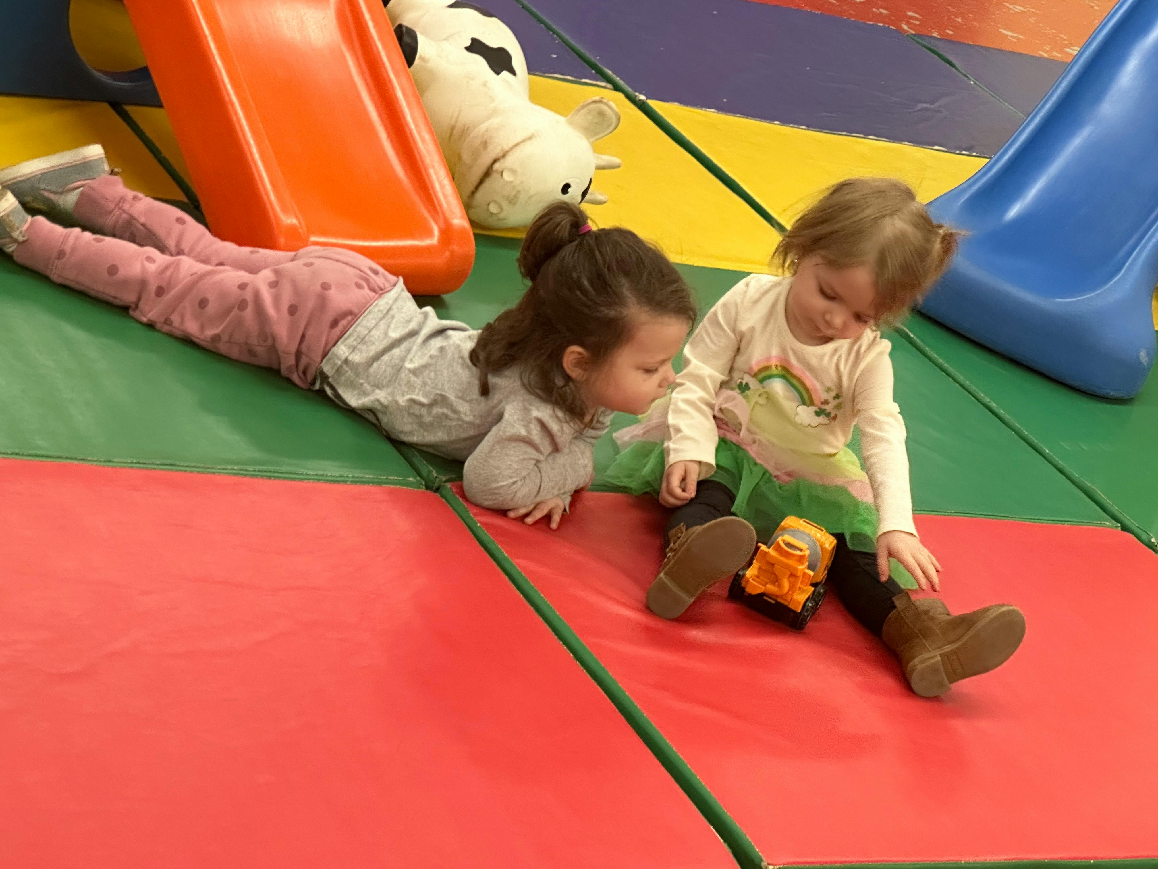 Two children playing on a soft play mat with slides