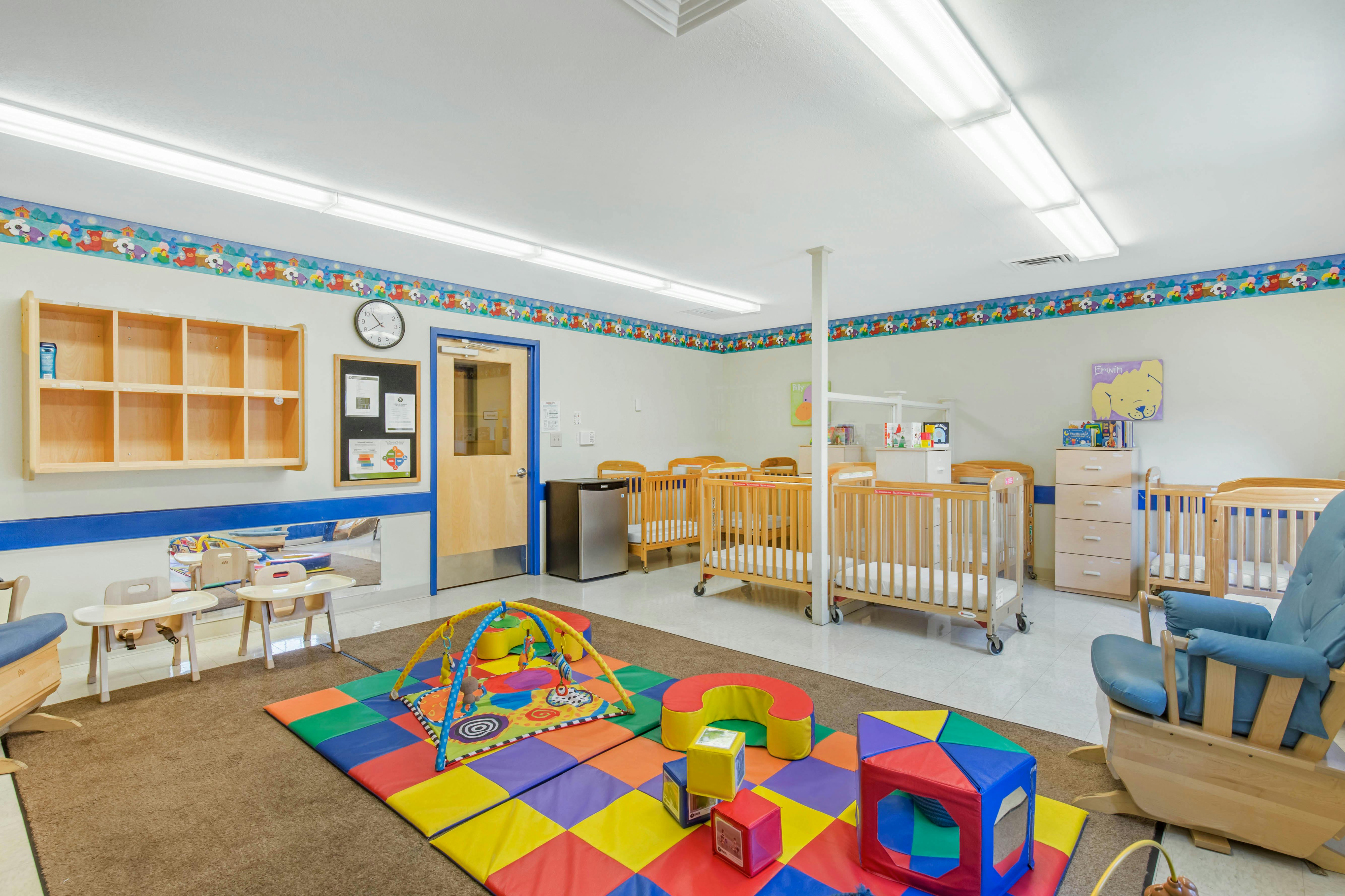 Baby nursery with multiple cribs, a playmat on the floor, and a wooden rocking chair