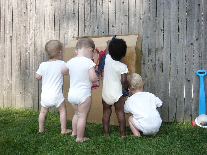 Four children painting on a cardboard box outdoors